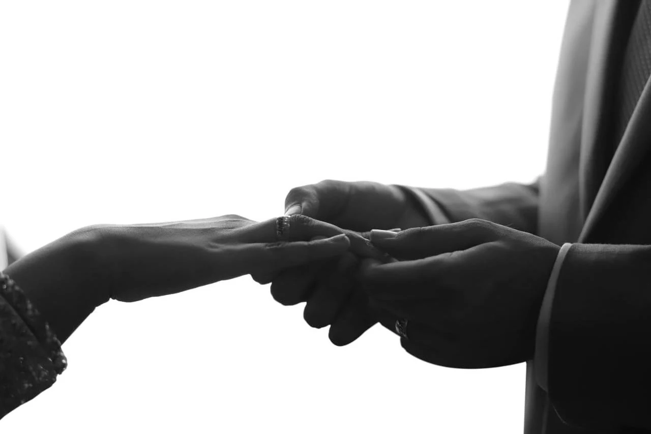Black-and-white close view of two hands meeting against a bright window