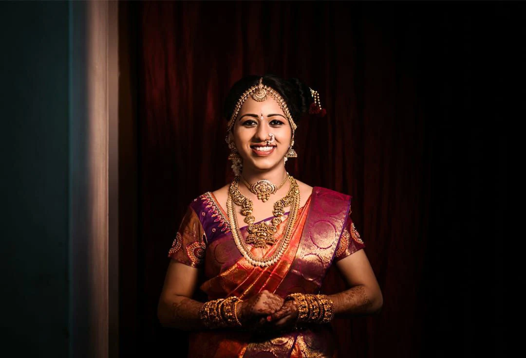 A woman smiling in warm light against a dark curtain