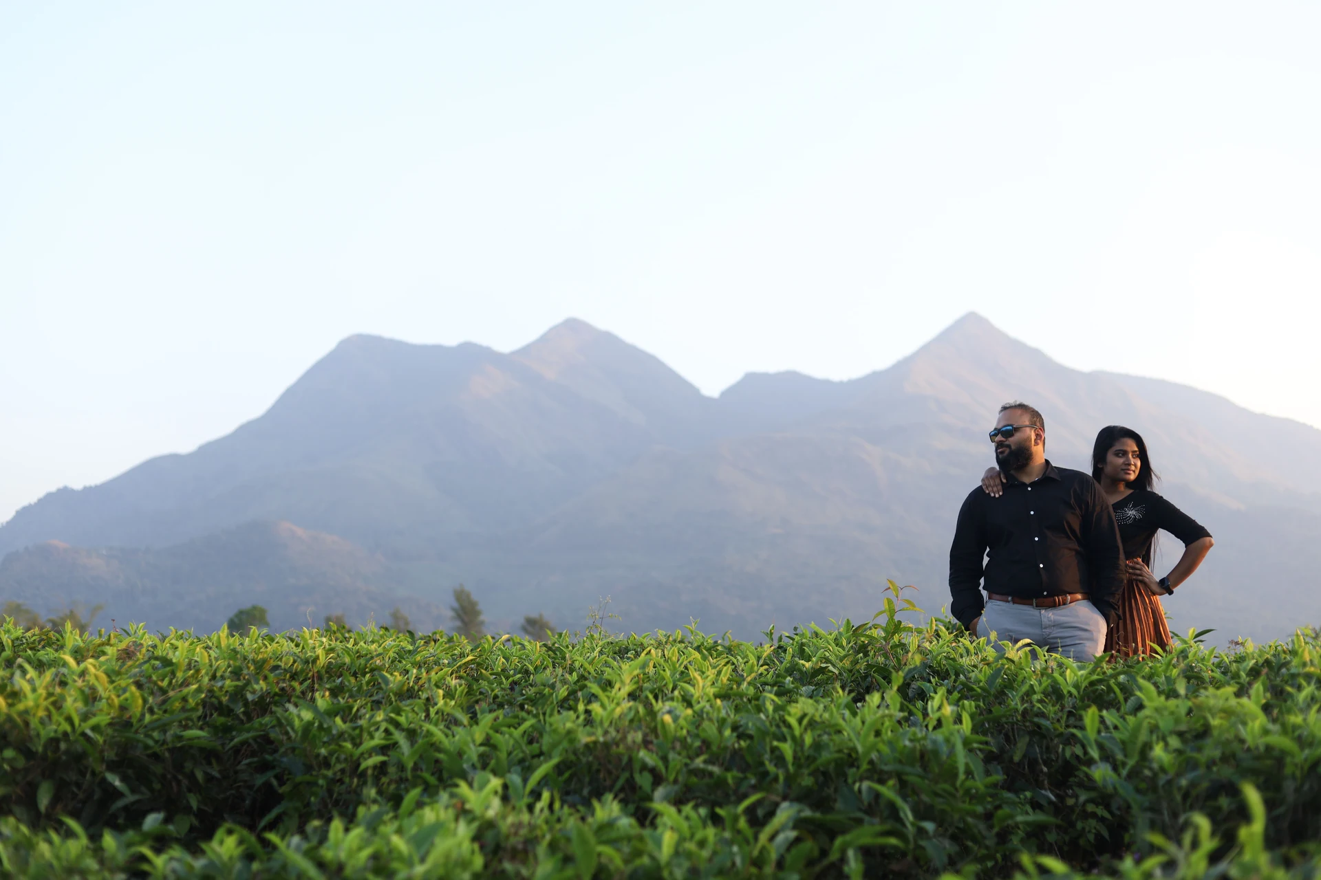 Couple standing above green foliage with mountains behind them