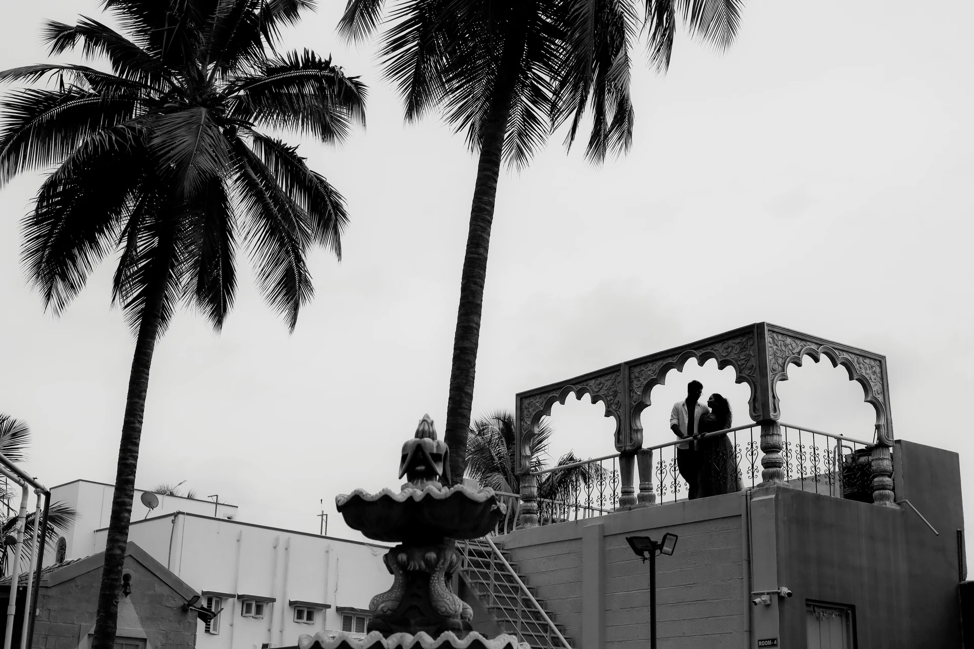 A couple on a balcony framed by palm trees in black and white