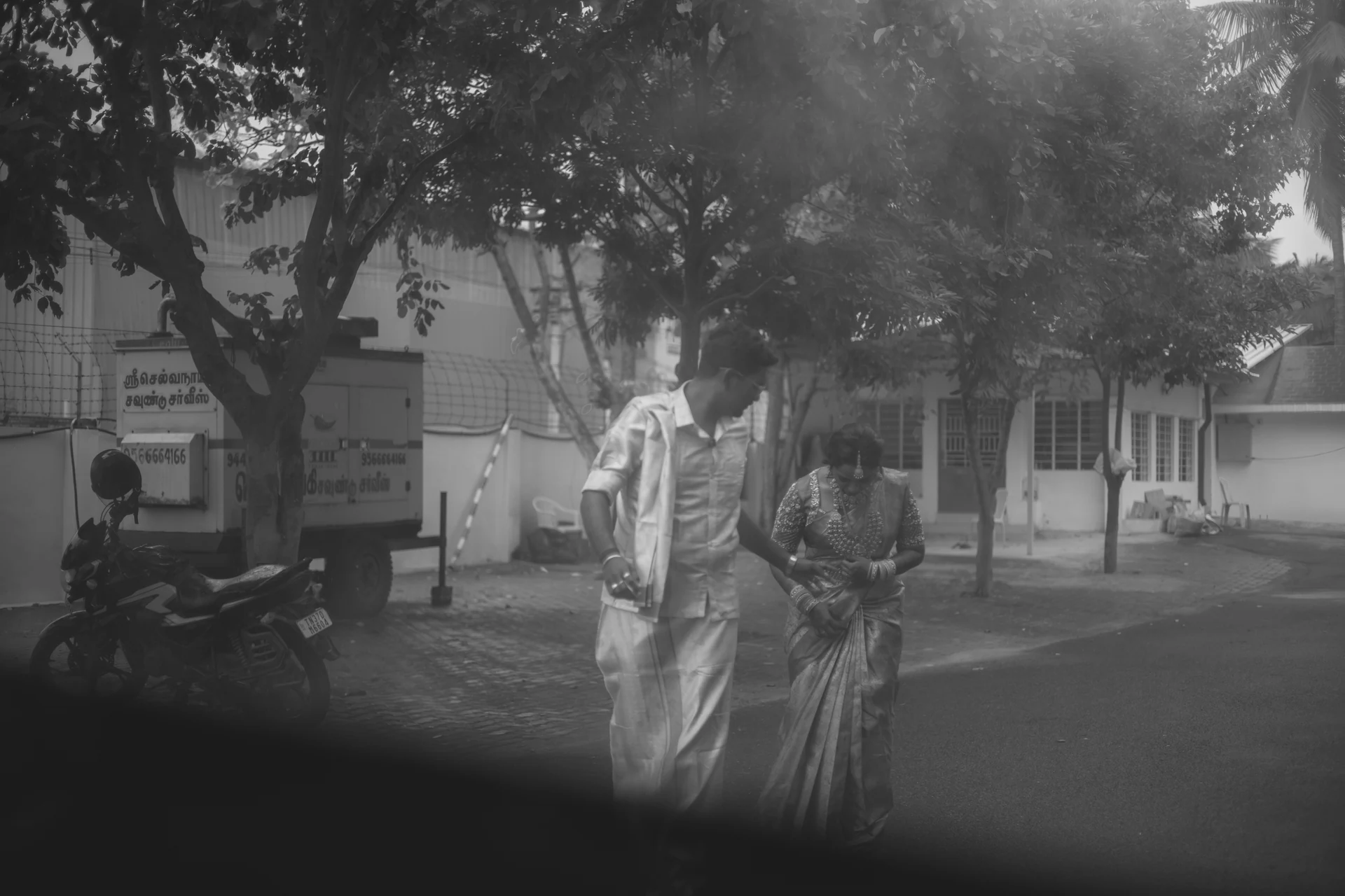 Black-and-white portrait of a couple walking beneath trees