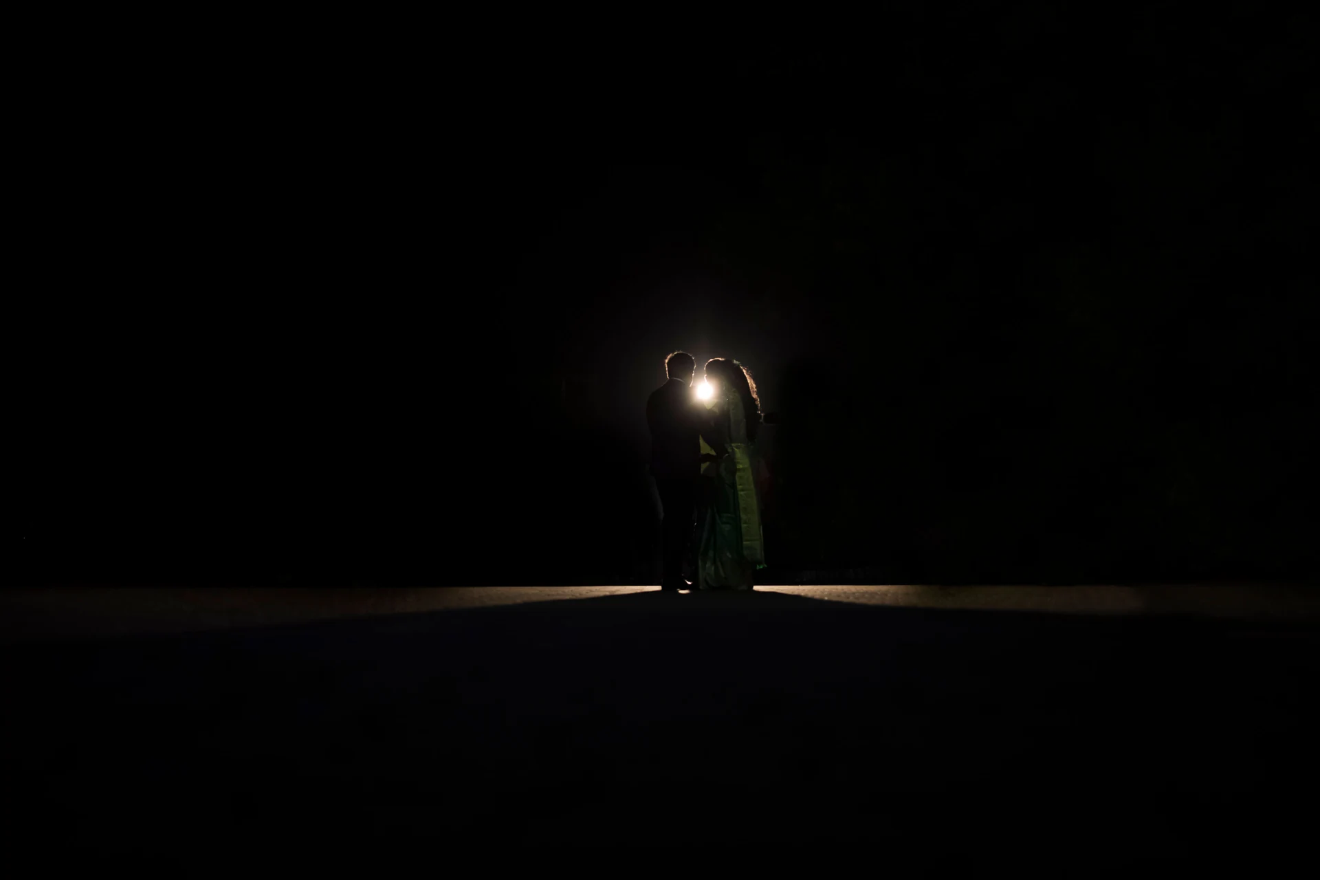 Two figures standing beneath a small pool of light in the dark