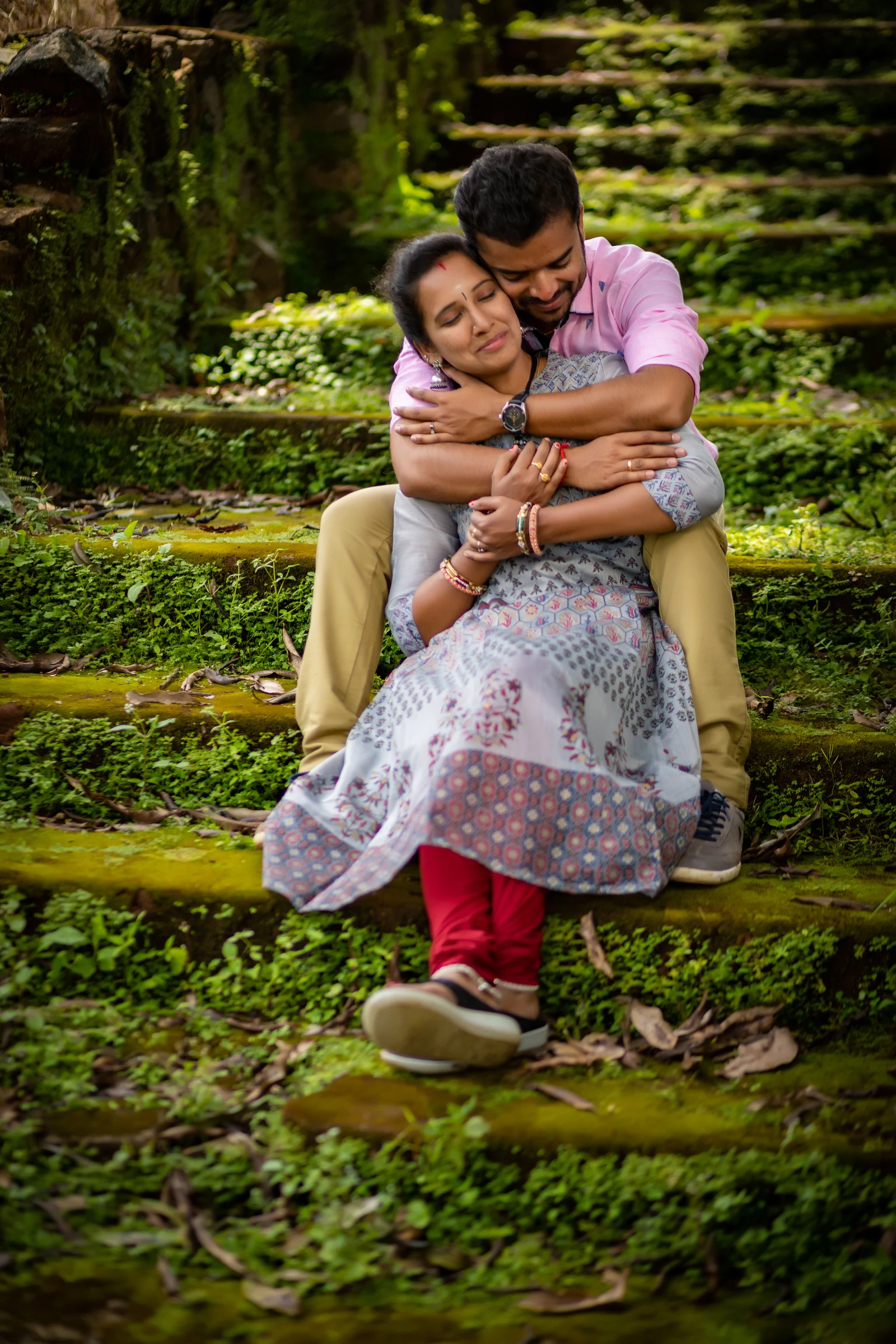 Couple embracing while seated on moss-covered steps