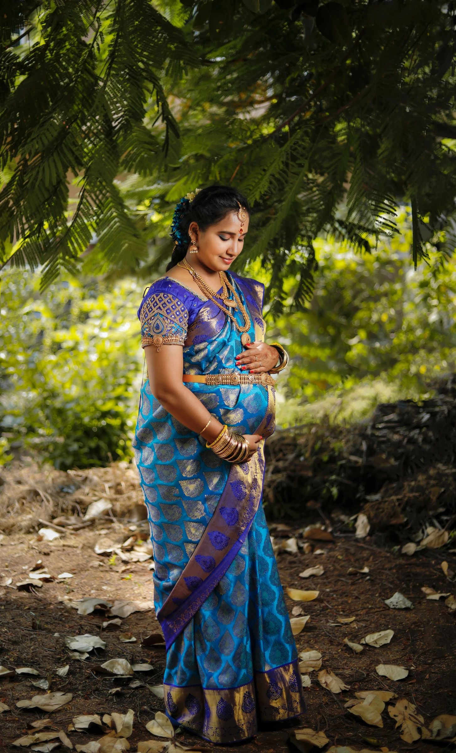 A woman in a blue sari standing beneath trees