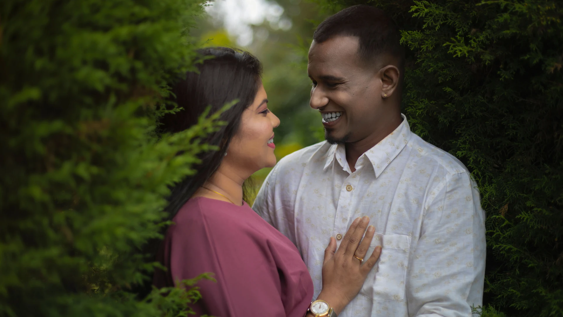 Couple smiling at each other through green foliage