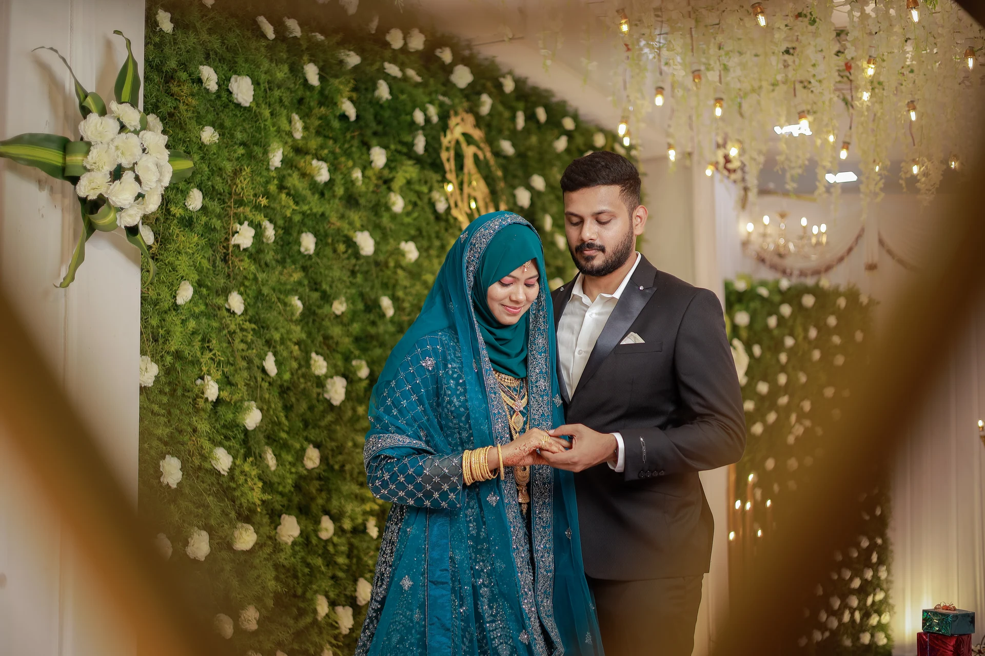 Couple looking down together in front of greenery and small lights