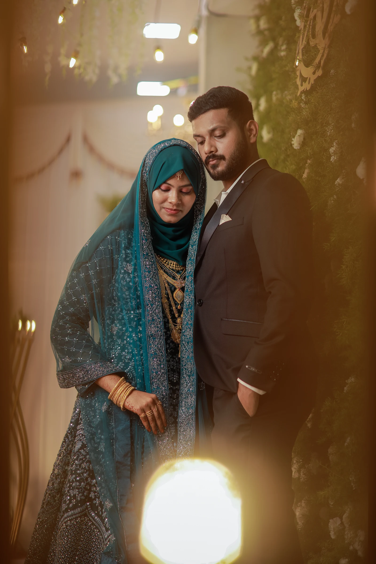 Couple standing close together in a corridor, framed by warm lights